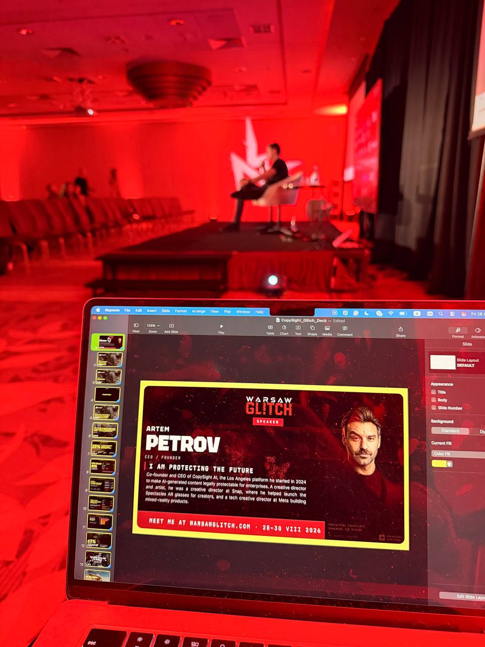 A laptop showing Artem Petrov's Warsaw Glitch speaker card in the CopySight deck, in front of a red-lit stage